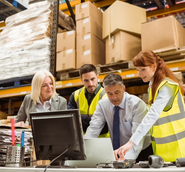 Four warehouse professionals collaborating around laptop computer in distribution center