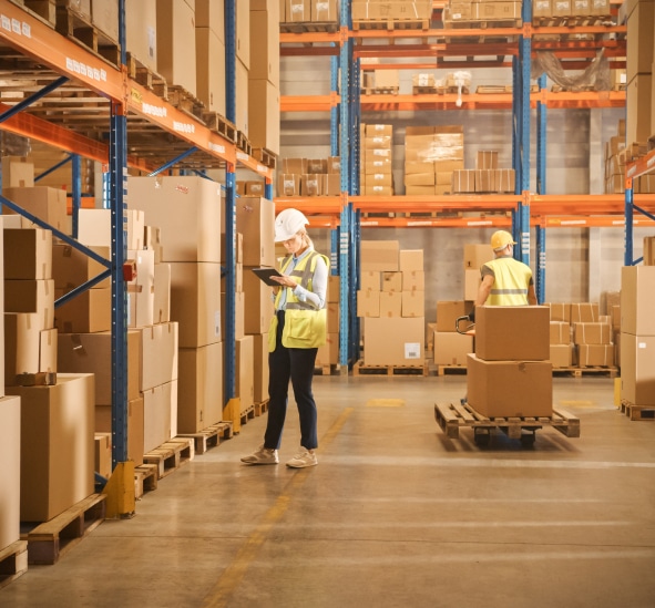 Warehouse workers in safety vests managing inventory with pallet jack and shelving