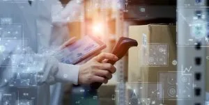 person holding an RF scanner in front of a box with a barcode while holding a tablet
